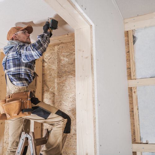 General Construction Contractor Attaching Drywall Using Cordless Drill Driver. Caucasian Remodeling Worker in His 40s.